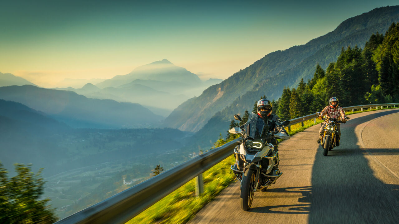 Zwei Motorräder auf einer Bergstraße, Nebel liegt im Tal, dahinter ein Gipfel